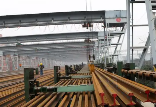 鐵路工人用鋼絲繩電動葫蘆將鋼軌吊裝到存軌臺座上